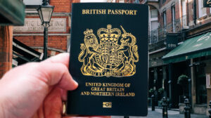 A hand lifts up a modern dark blue British passport in a central London street lined with restaurants.